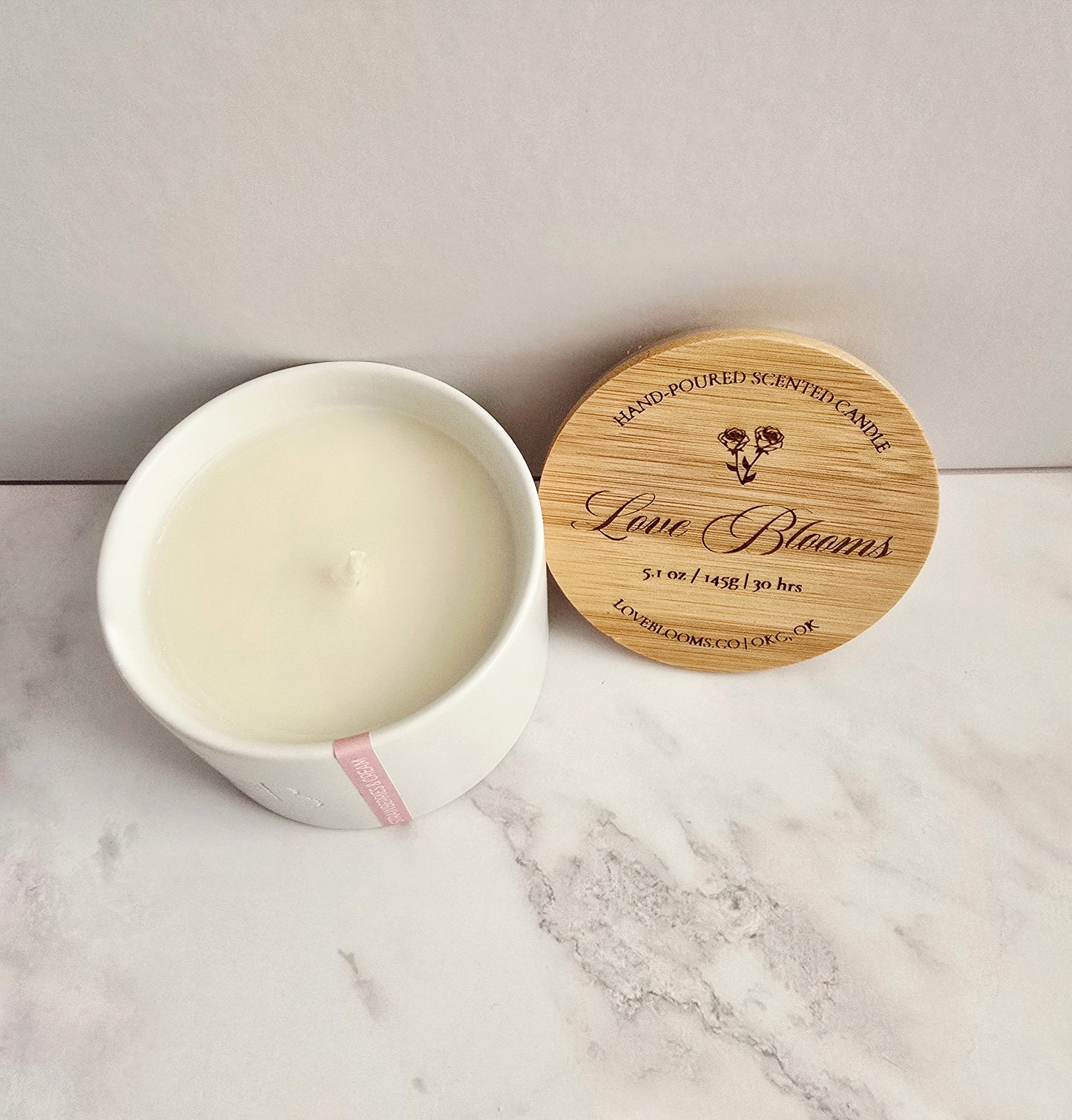 Candle in a white container with a wooden lid on a marble surface