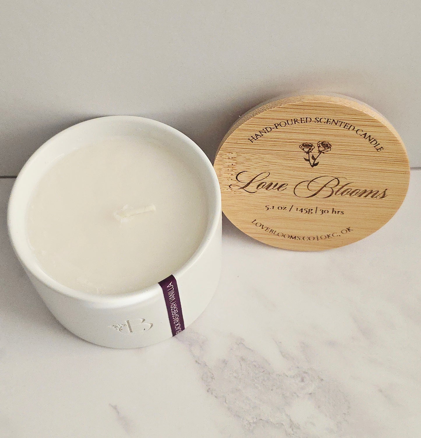 White candle in a ceramic container with a wooden lid on a marble surface