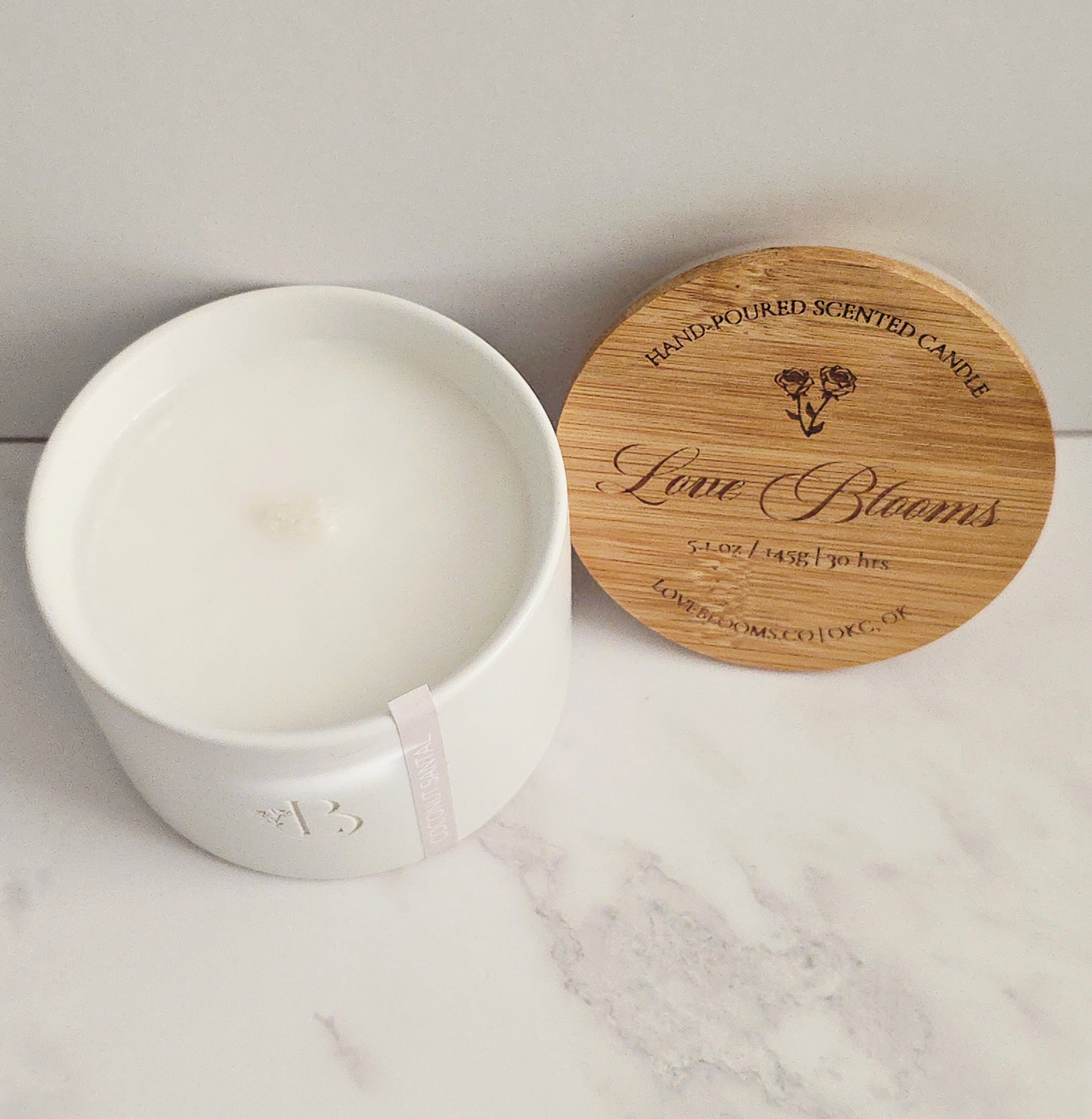 White candle in a container with a wooden lid on a marble surface