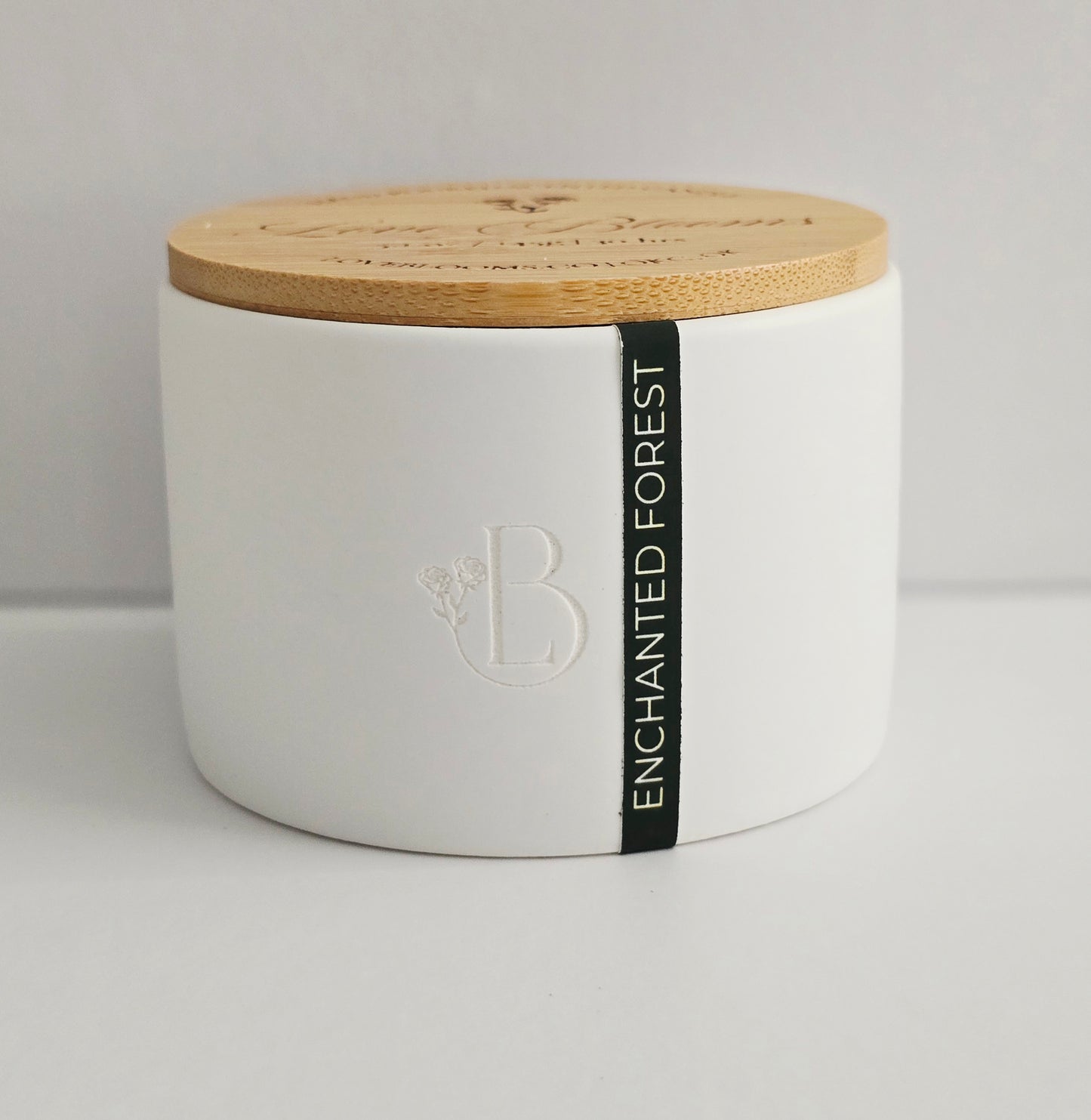 White candle jar with wooden lid and 'Enchanted Forest' label on a light gray background