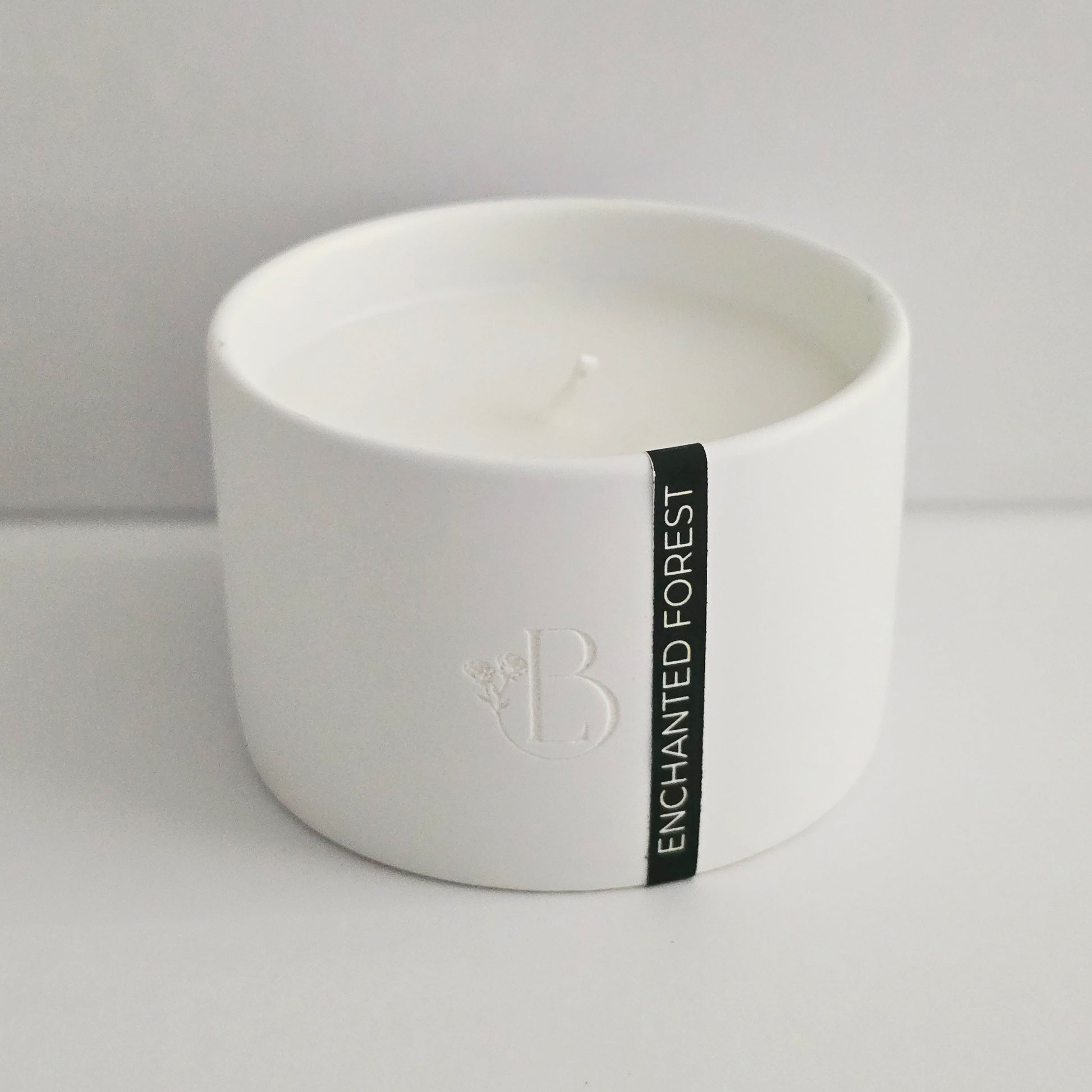 White candle in a bowl with 'Enchanted Forest' label on a light gray background