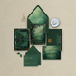 Green wedding invitation set on a textured beige surface with a pair of scissors and a small dish.