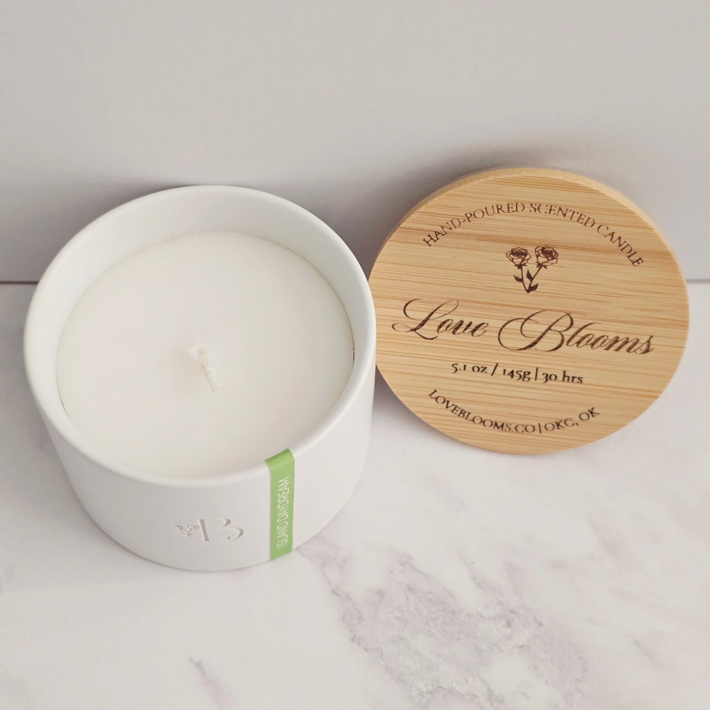 White candle in a white container with a wooden lid on a marble surface