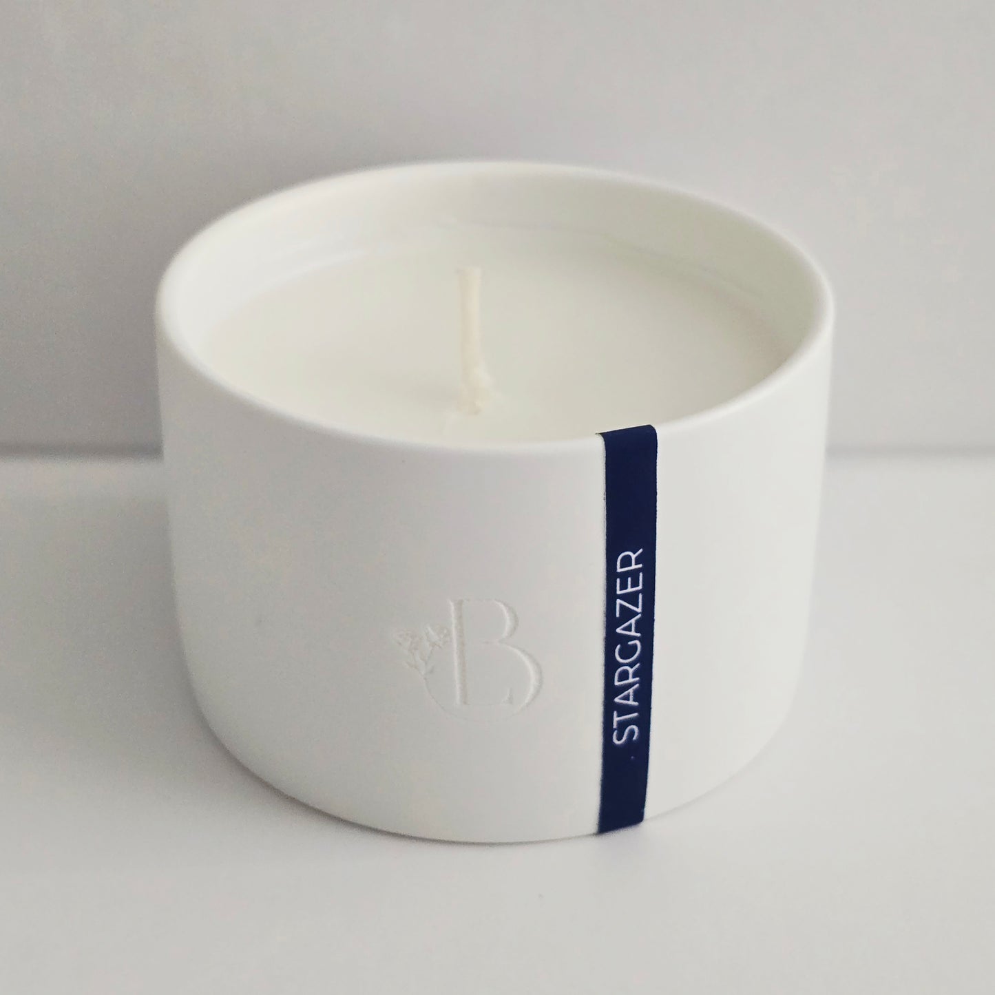 White candle in a ceramic holder with 'Stargazer' text on a light gray background