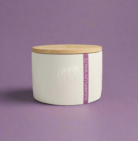 White candle jar with wooden lid and 'Sugarplum Waltz' label on a light background