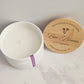 Hand-poured scented candle in a white container with a wooden lid on a marble surface.