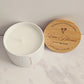 White candle in a container with a wooden lid on a marble surface