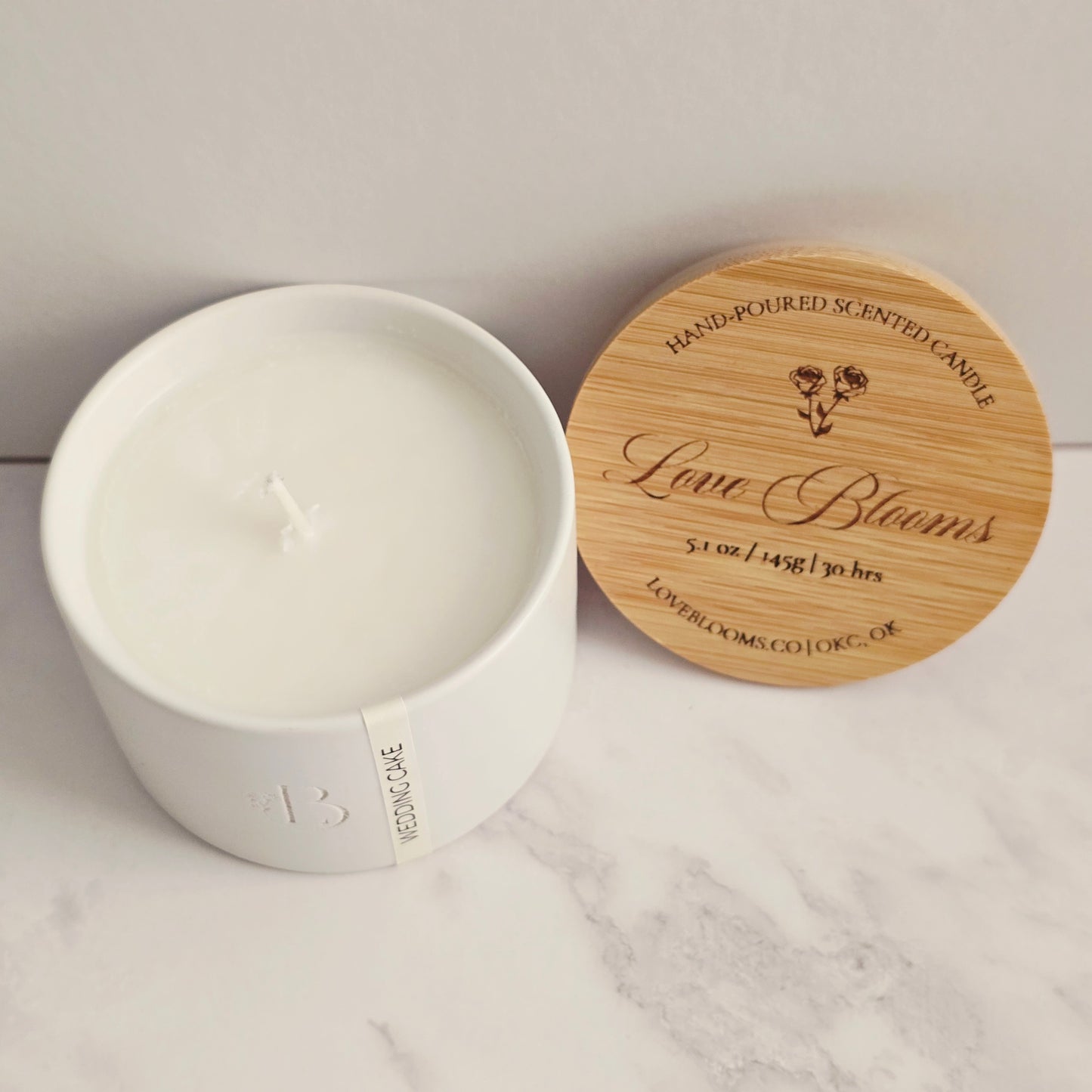 White candle in a container with a wooden lid on a marble surface