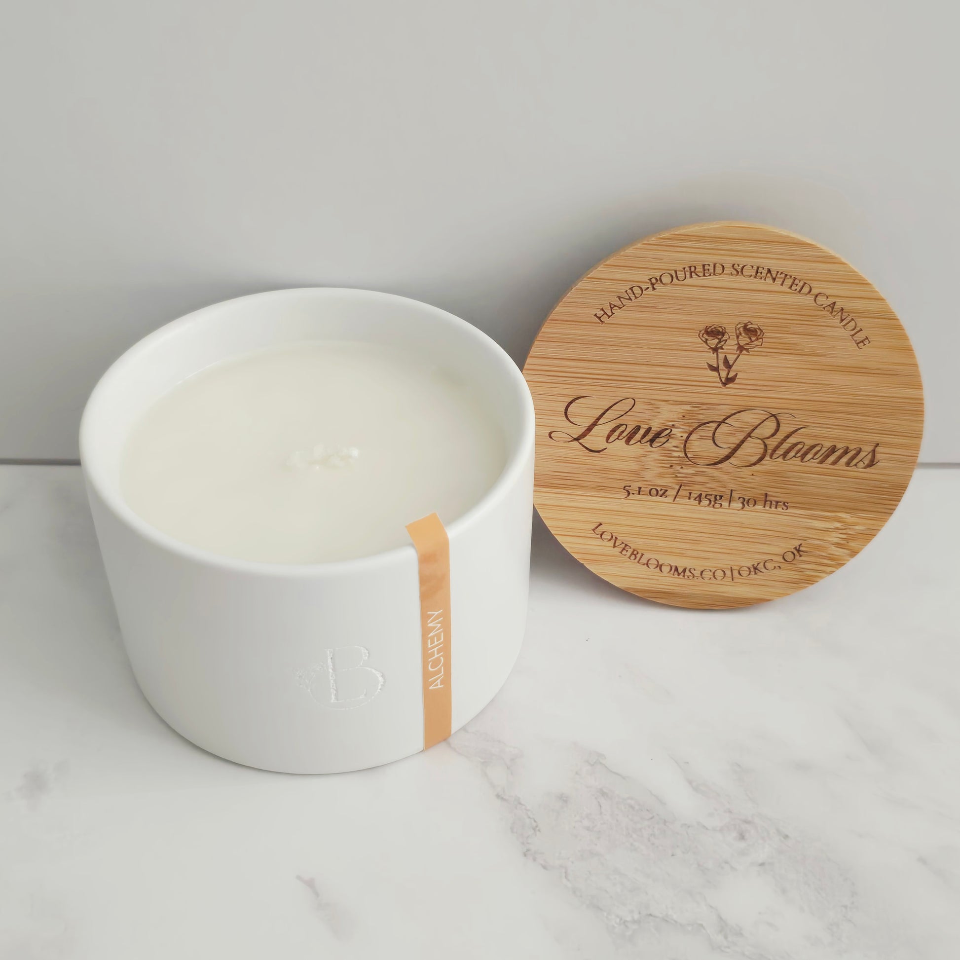 White candle in a white container with a wooden lid on a marble surface