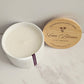 White candle in a ceramic container with a wooden lid on a marble surface