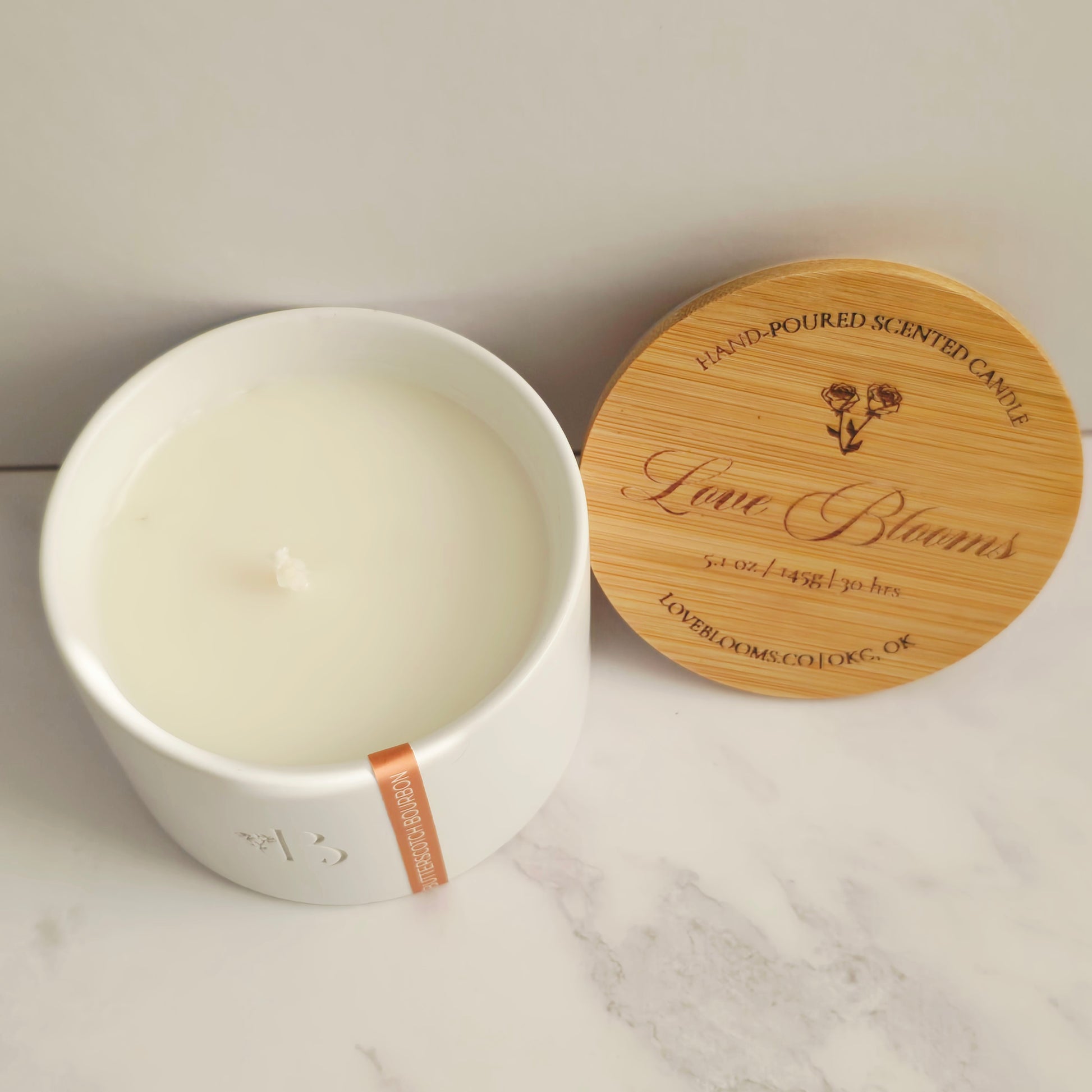 White candle in a white container with a wooden lid on a marble surface