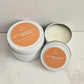 Butterscotch-scented candles in white tins on a marble surface