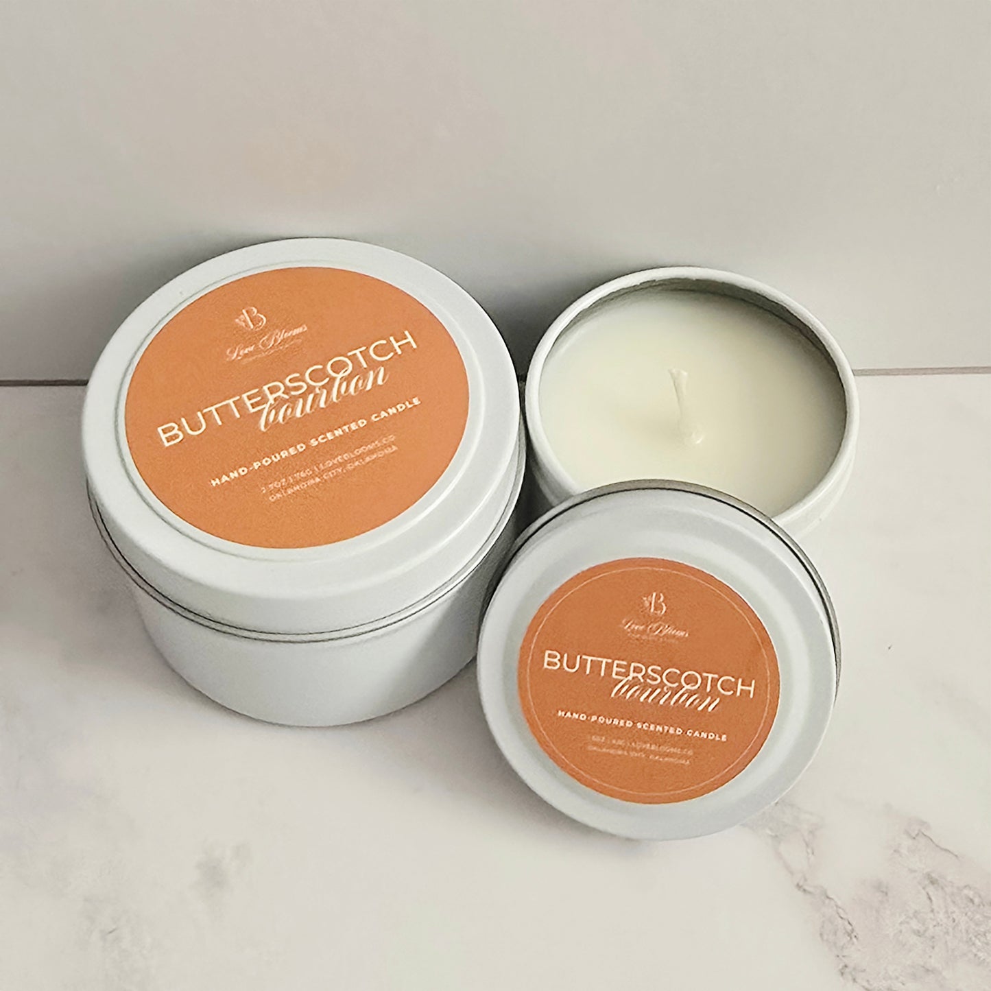 Butterscotch-scented candles in white tins on a marble surface