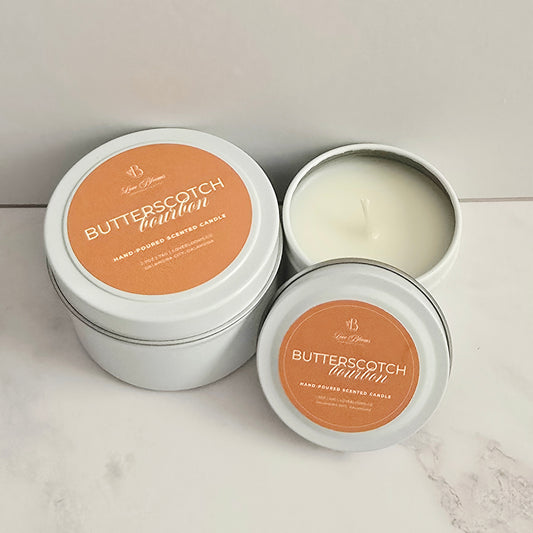 Butterscotch-scented candles in white tins on a marble surface