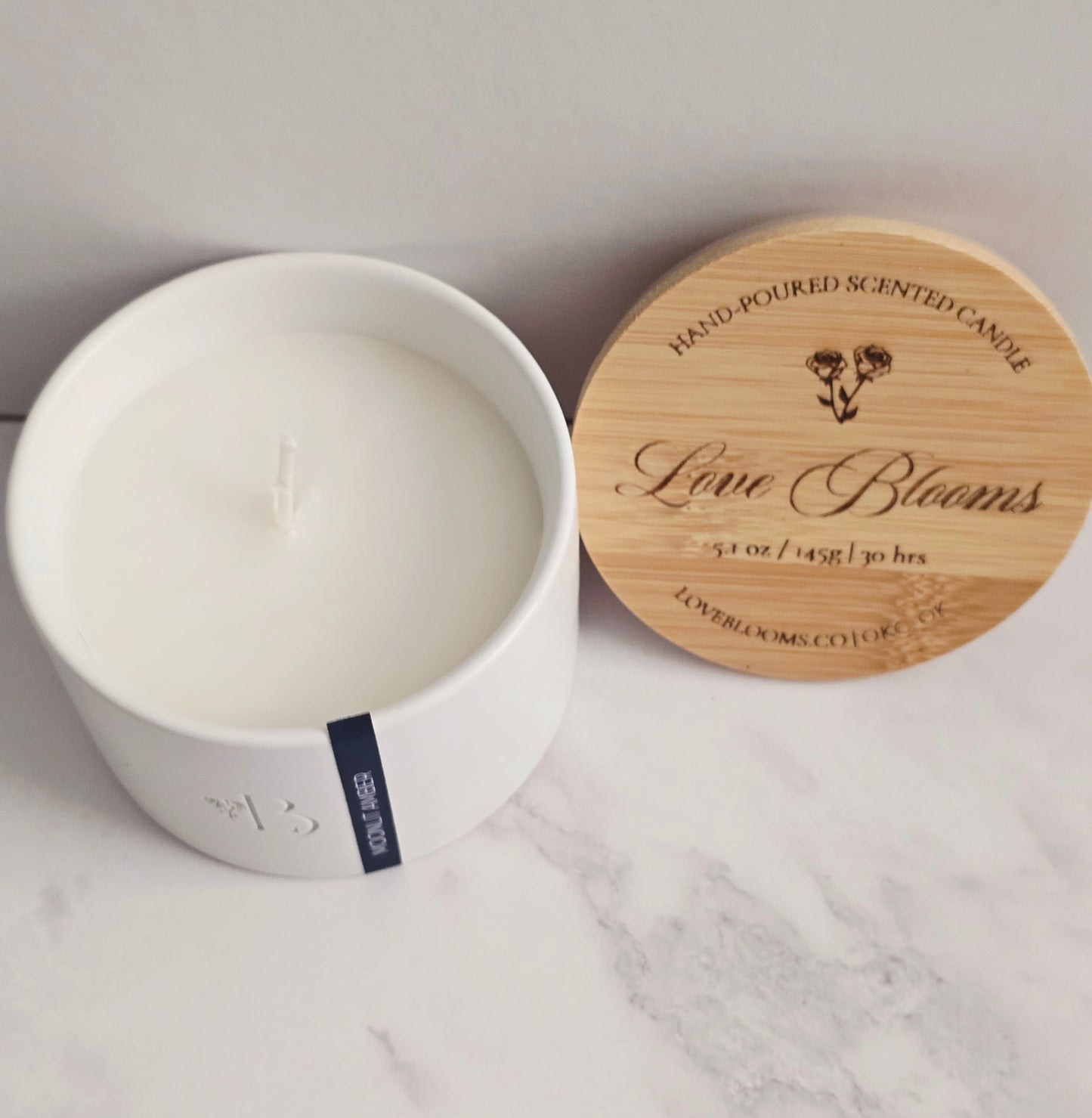 Candle in a white container with a wooden lid on a marble surface