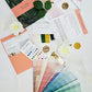 Color swatches, stationery items, and flowers on a white surface
